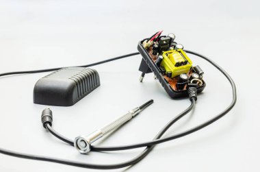 Parçalanmış bir telefon şarj aletinin iç parçaları. Şarj cihazının siyah plastik kutusu açıldı, devre kartı, transformatör (belirgin sarı bileşen), kondansatörler, rezistörler ve diğer elektronik bileşenler ortaya çıktı.