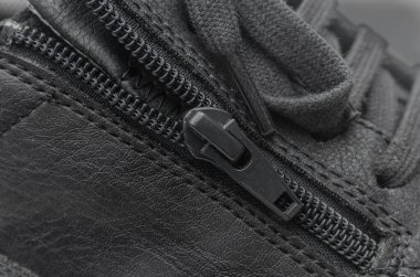 Siyah deri ayakkabılı siyah bir fermuarın yakın plan makro görüntüsü, kumaşın dokusunu ve bağlayıcının detaylarını vurguluyor..