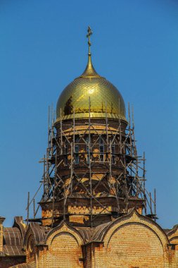 Ortodoks kilisesinin, açık mavi gökyüzüne karşı ahşap iskelelerle çevrili altın kubbesinin detaylı bir görüntüsü..