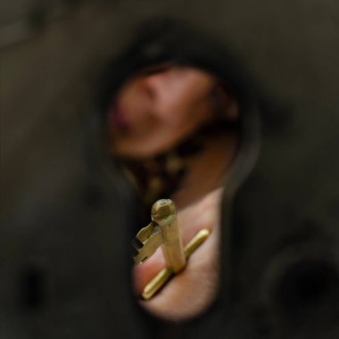 Eski moda pirinç anahtarı tutan bir elin yakın plan görüntüsü, büyük bir anahtar deliğinden görülüyor, gizem ve beklenti hissi yaratıyor..