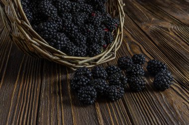 Olgun, koyu böğürtlenlerden oluşan yakın çekim zengin, ahşap bir yüzeye dökülen bir sepet, yaz hasadının tazeliğini ve bolluğunu vurguluyor..