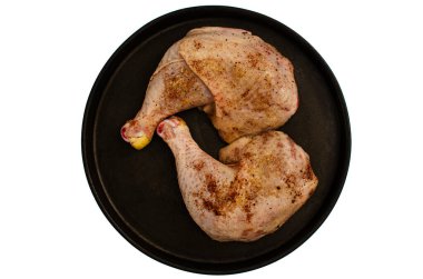 İki çiğ, terbiye edilmiş tavuk budu. Koyu, dökme demir bir tavada, temiz beyaz arka planda. Kümes hayvanları baharatlarla serpilmiş ve pişirilmeye hazır..