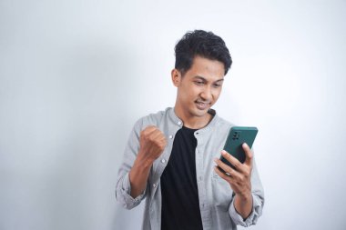 Heyecanlı bir gencin portresi beyaz arka planda izole edilmiş bir şekilde cep telefonuna bakıyor.