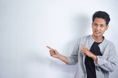 Yakışıklı Asyalı genç adam, izole edilmiş arka planda bir ürün sunmak için kenarı işaret ediyor.