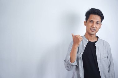 Yakışıklı Asyalı genç adam, izole edilmiş arka planda bir ürün sunmak için kenarı işaret ediyor.