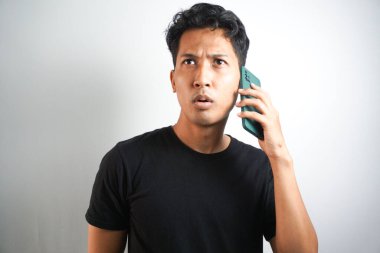Genç Asyalı adamın telefonu aradığında kafası karışıyor ve şoka giriyor. Siyah gömlek giyen Endonezyalı adam..