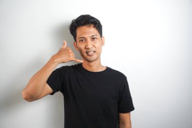 Genç adam gülümsüyor. İnsanların yaşam tarzı konsepti. İşaret parmağını kameraya doğru hareket ettiriyor ve beni ara diyor. Beyaz arka planda kapalı bir stüdyo resmi..