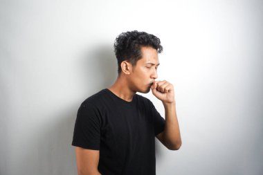 Boğazı ağrıyan ve grip belirtileri gösteren genç bir adam. Ağzı beyaz duvara dayalı öksürüyor.