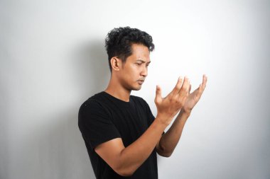 Genç yakışıklı adam siyah tişört giyerek dua ediyor. Beyaz arkaplan karşısında izole kişi.