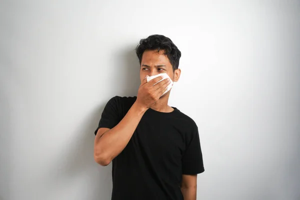 stock image young man has allergies coughs and sneezes is allergic to dust irritates his nasopharynx uses tissues to cover his snot : Asian man in poor health suffers from a respiratory disease.