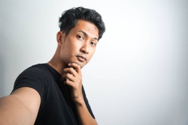 Yakışıklı genç adam sıradan kıyafetler giyiyor telefonuyla selfie çekiyor.