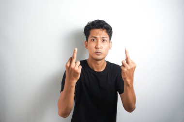 Arrogant and careless asian man in black t-shirt dont give a fuck, showing middle fingers at camera and frowning, standing over white background