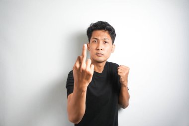 Arrogant and careless asian man in black t-shirt dont give a fuck, showing middle fingers at camera and frowning, standing over white background