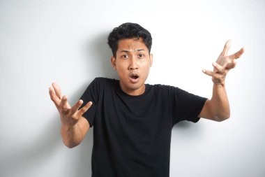 Gri arka planda siyah gömlekli Asyalı adamın şok olmuş yüzü..