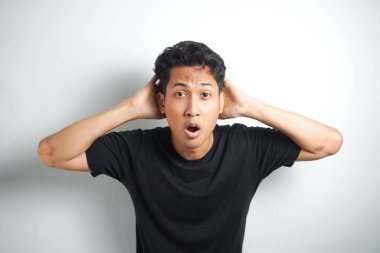 Gri arka planda siyah gömlekli Asyalı adamın şok olmuş yüzü..