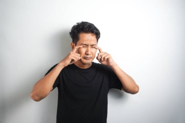 Asyalı genç adam ağlıyor ve parmaklarıyla gözyaşlarını siliyor.