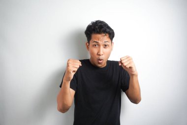 Asyalı heyecanlı bir adam beyaz arka planda iki yumrukla başarıyı kutluyor. Yakın çekim, stüdyo çekimi, mutluluk, olumlu duygu ve his. Yaptım bile. yüz ifadesi