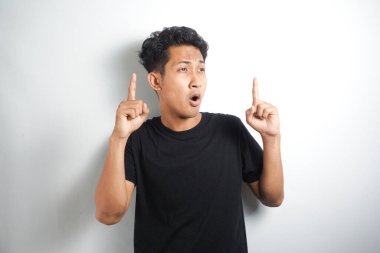 Mavi tişörtlü heyecanlı genç adam, parmağıyla yukarı bakıyor, harika bir fikri var, beyaz arka planda izole edilmiş.