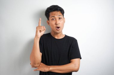 Mavi tişörtlü heyecanlı genç adam, parmağıyla yukarı bakıyor, harika bir fikri var, beyaz arka planda izole edilmiş.