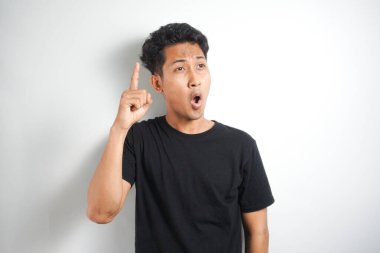 Mavi tişörtlü heyecanlı genç adam, parmağıyla yukarı bakıyor, harika bir fikri var, beyaz arka planda izole edilmiş.