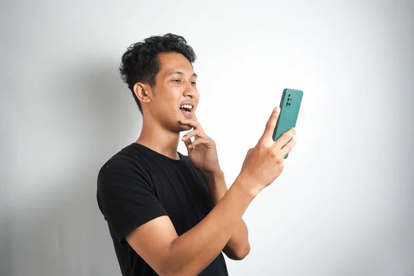 stock image Young man smiling while reading his smartphone. Portrait of smiling man reading message with smartphone in white background.