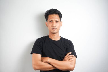 Mutlu genç adam. Siyah tişörtlü yakışıklı bir gencin portresi. Kollarını kavuşturup gülümsüyor ve beyaz arka planda duruyor.