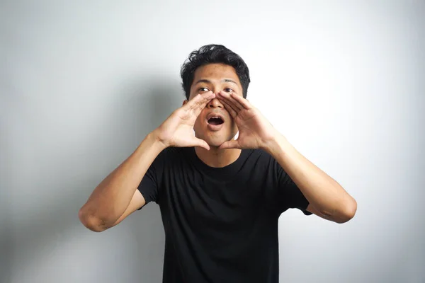 stock image Young man keeping hand near mouth and screaming. Handsome happy man wearing black T-shirt, guy speaking loudly, isolated on white background