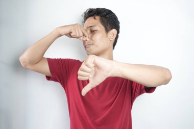 Tiksinmiş Asyalı genç adam elleriyle burnunu kapatıyor.