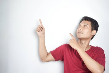 Portrait of a happy young man in white t-shirt pointing fingers away at copy space isolated over white background