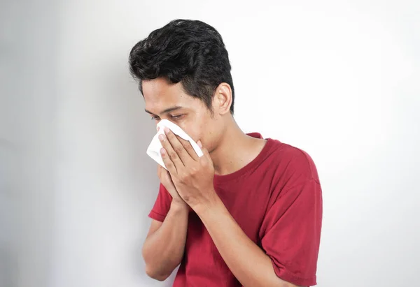 Asian man covers his mouth and nose with a tissue because he feels sick with the flu.