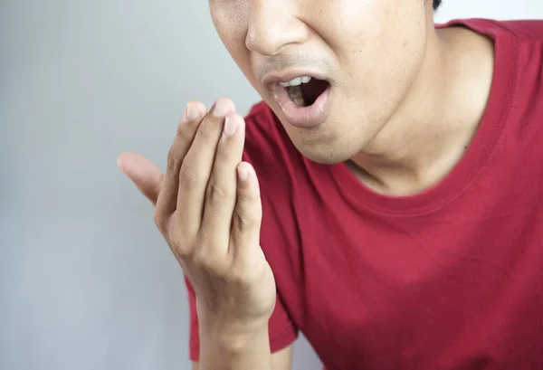 A man checks for bad breath and breathes with his hands. he has bad breath Concept of oral and dental health