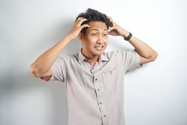Horizontal photo of good-looking asian man pictured isolated on white background showing how much his head hurts, experiencing pain, looking miserable and exhausted