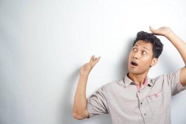 Young asian man wearing shirt and shouting wow by pointing right with his finger isolated on white background with copy space for your text.