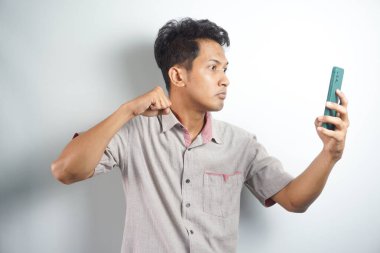 Young asian man angry, frustrated and furious with his phone, angry with customer service over white background.