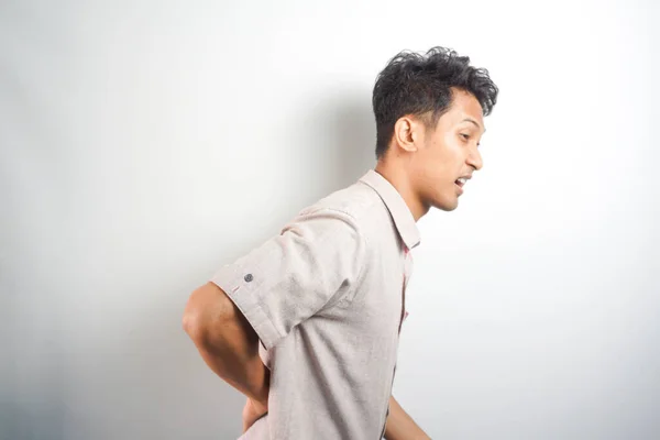 Young asian young man suffering from backache for having made an effort on isolated background.