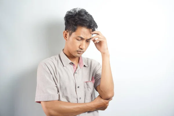Horizontal photo of good-looking asian man pictured isolated on white background showing how much his head hurts, experiencing pain, looking miserable and exhausted