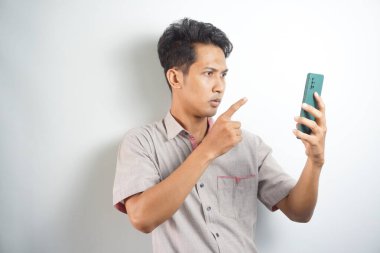Young asian man angry, frustrated and furious with his phone, angry with customer service over white background.