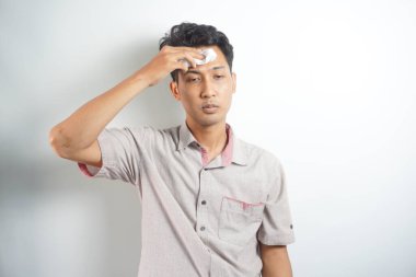 Beyaz stüdyo arka planında izole edilmiş aşırı ısınmış terli genç adam kağıt peçete kullanarak sıcak çarpmasından ya da yüksek sıcaklıktan muzdarip. Kafadan yakından çekilen portre yorgun milenyum çocuğu kendini sağlıksız hissediyor..