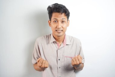 excited Asian man celebrating success with two fists in air isolated on the blue background. close up portrait, studio shot , happiness, positive emotion and feeling. I've done it. facial expression