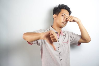 portrait of disgusted man pinches nose with fingers hands looks with disgust something stinks bad smell situation isolated on white wall background. Human face expression body language reaction