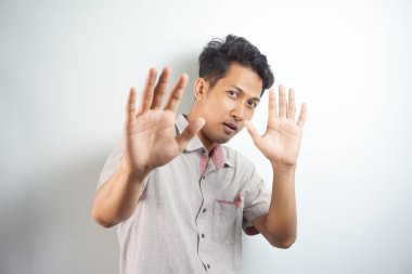 Attractive young asian man making fearful gestures with palms, defending himself from someone, asking to stop him immediately. Guy says stay away from me, show stop sign. Body language concept