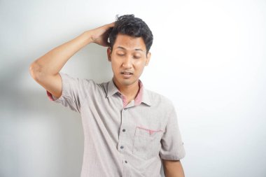 Horizontal photo of good-looking asian man pictured isolated on white background showing how much his head hurts, experiencing pain, looking miserable and exhausted