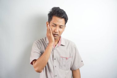 Diş ağrısı konsepti. Kapalı alanda, acı çeken genç bir erkeğin kötü diş ağrısından muzdarip yanağını tutarken, acı dolu bir ifadeyle kameraya bakarken.