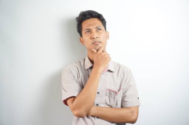 Thoughtful male customer thinking hard, looking away at copy space, leaning chin on hand. Handsome young man in casual shirt isolated over white background. Special offer concept