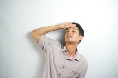 Horizontal photo of good-looking asian man pictured isolated on white background showing how much his head hurts, experiencing pain, looking miserable and exhausted
