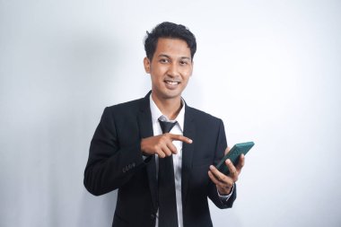 Portrait of a happy Asian young man wearing a suit while pointing at a mobile phone