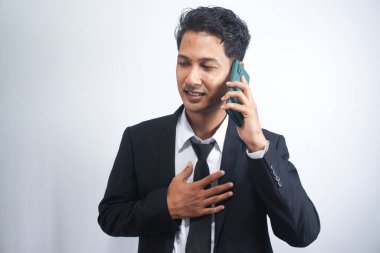 asian man in suit is on the phone and smiling receiving happy news, isolated on white background