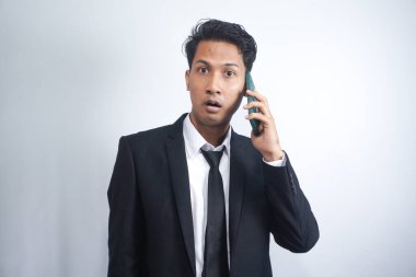 Genç Asyalı adamın telefonu aradığında kafası karışıyor ve şoka giriyor. Siyah gömlek giyen Endonezyalı adam..