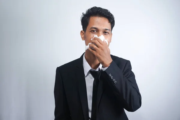 Horizontal portrait of unhealthy handsome man wearing suit, blowing nose into tissue. Male have flu, virus or allergy against white background. Healthy medicine and people concept