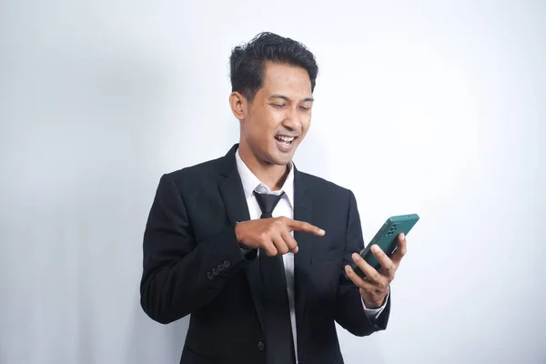 Portrait of a happy Asian young man wearing a suit while pointing at a mobile phone